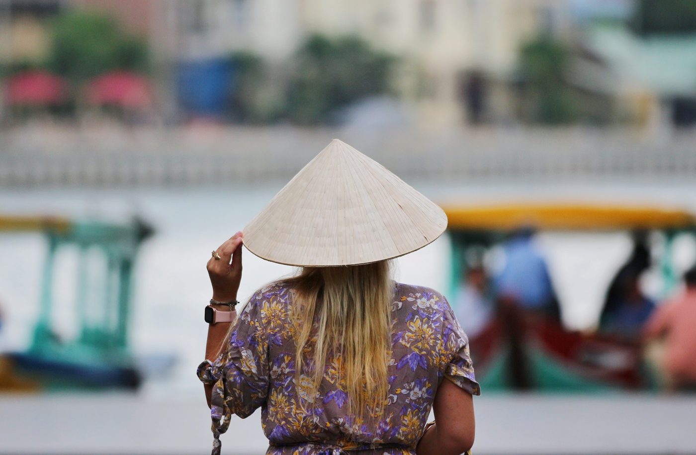 Woman wearing a traditional Vietnamese conical hat with blurred riverside boats in the background